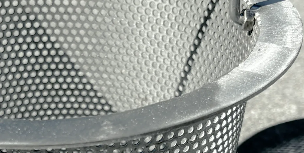 Flared top rim of a stainless steel skimmer basket in direct sun.