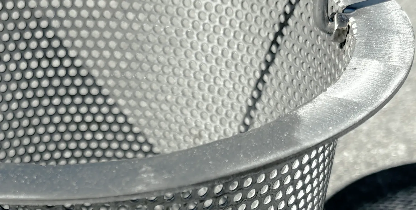 Flared top rim of a stainless steel skimmer basket in direct sun.
