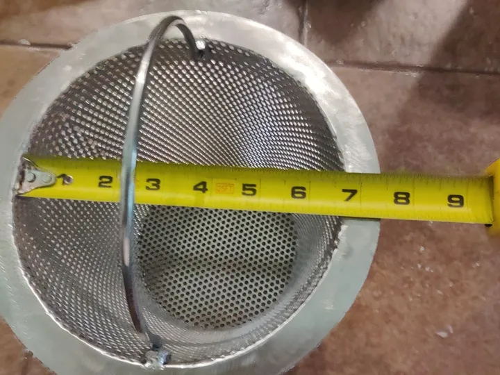 A tape measure laid across the top rim of a stainless steel skimmer basket.
