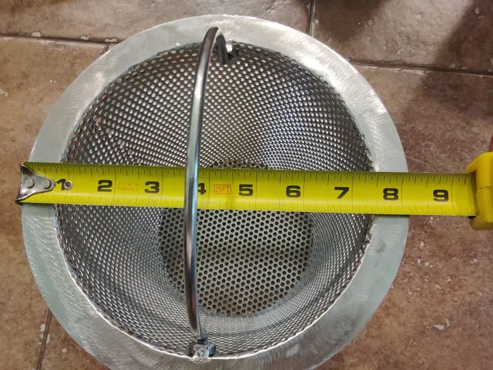 A tape measure at the edge of a stainless steel skimmer basket’s rim.